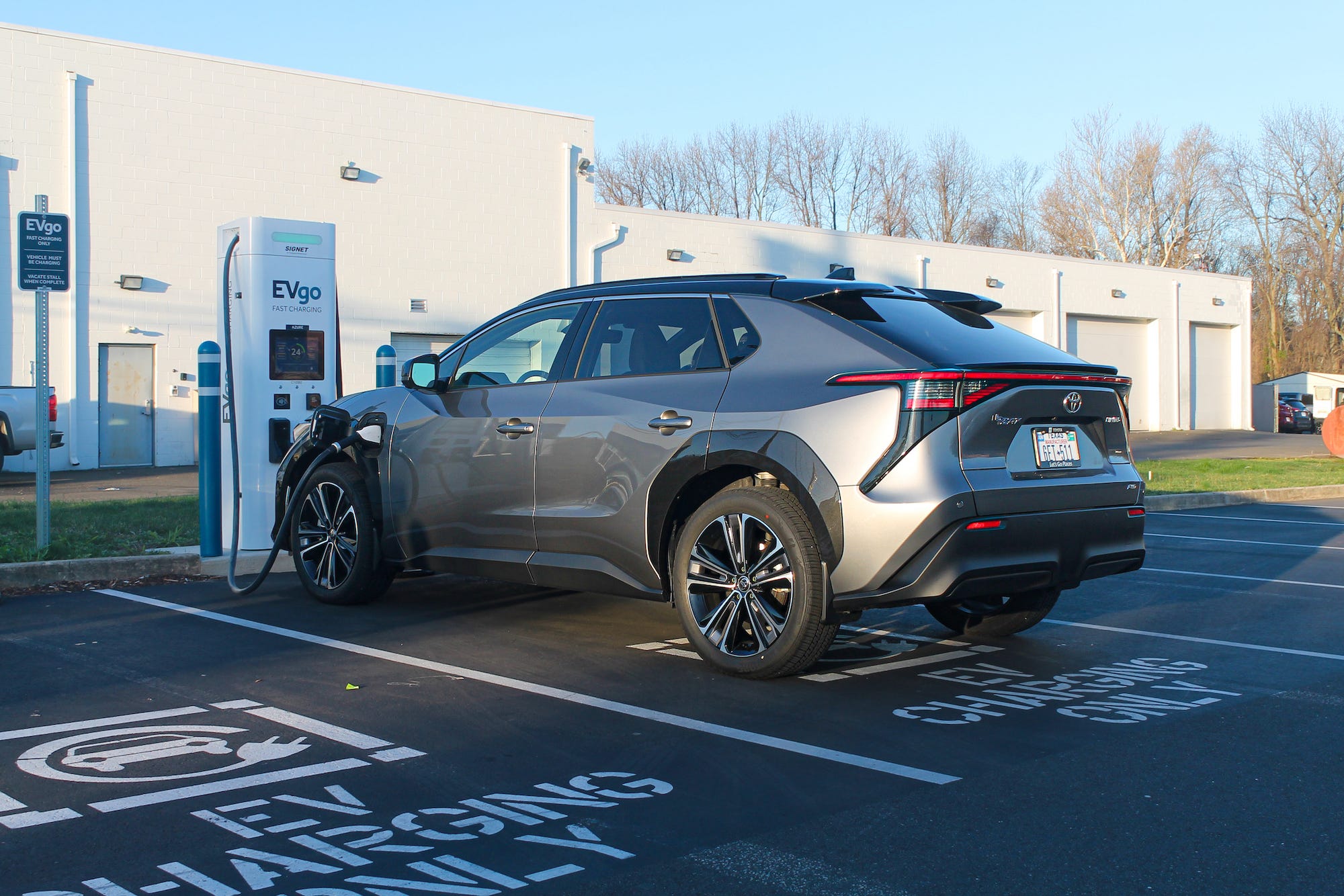 The 2023 Toyota bZ4X AWD Limited electric SUV sits in the shade, parked by a charging stall.
